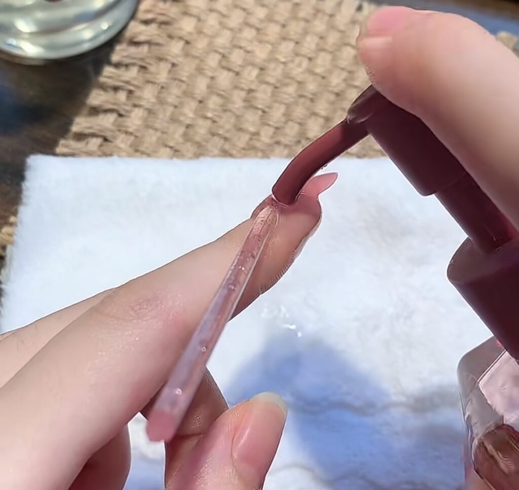 Use an orange wood stick to pry open the edge of the press-on nail and at the same time, squeeze a little bit of cleansing oil into the gap,